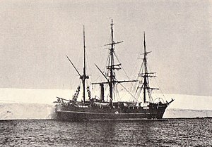 Three-masted ship with sails furled, lying next to a shelf of ice.